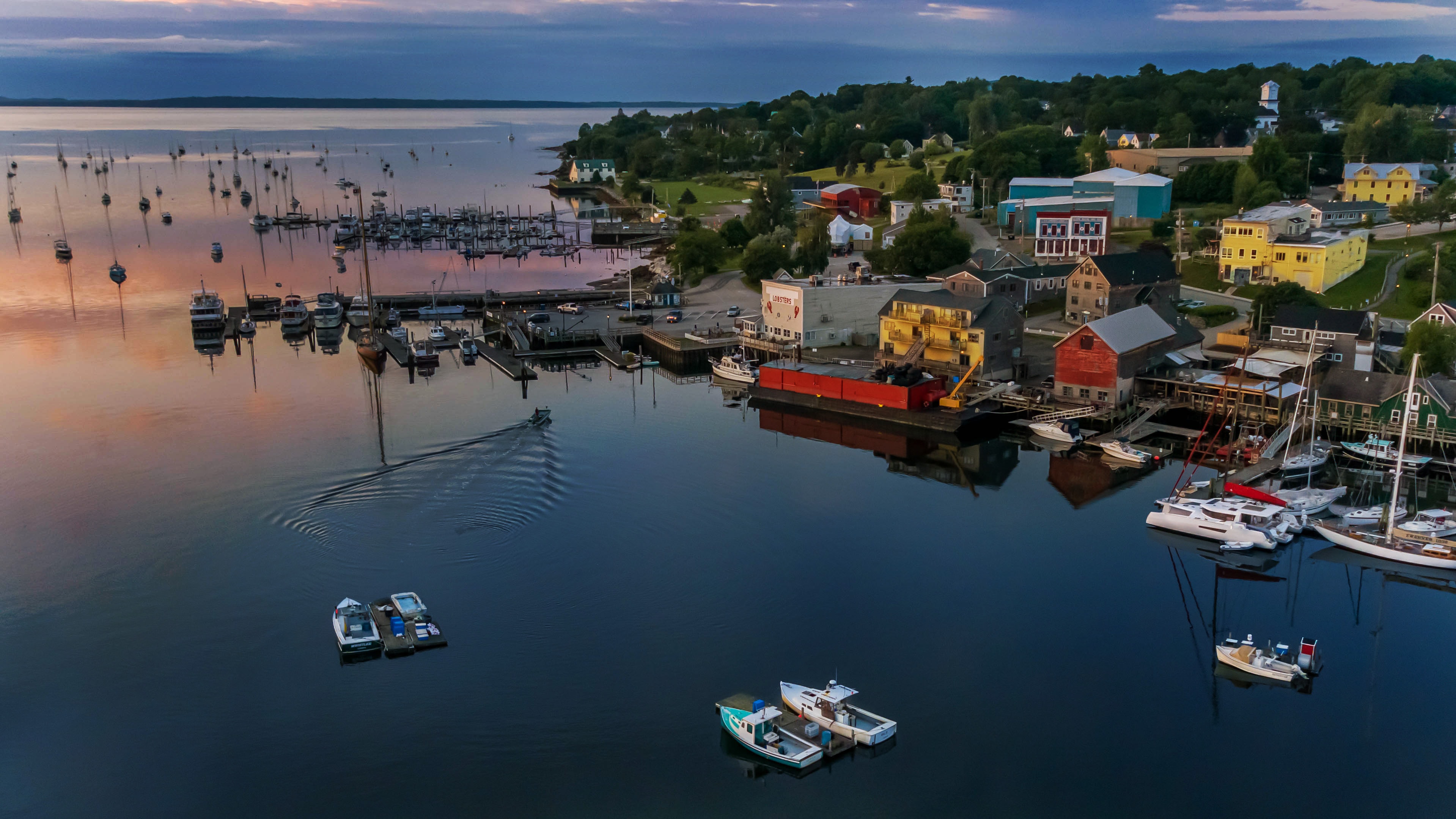 Aerial view of a Downeast Maine harbor at dawn, morning mist rolling over still water